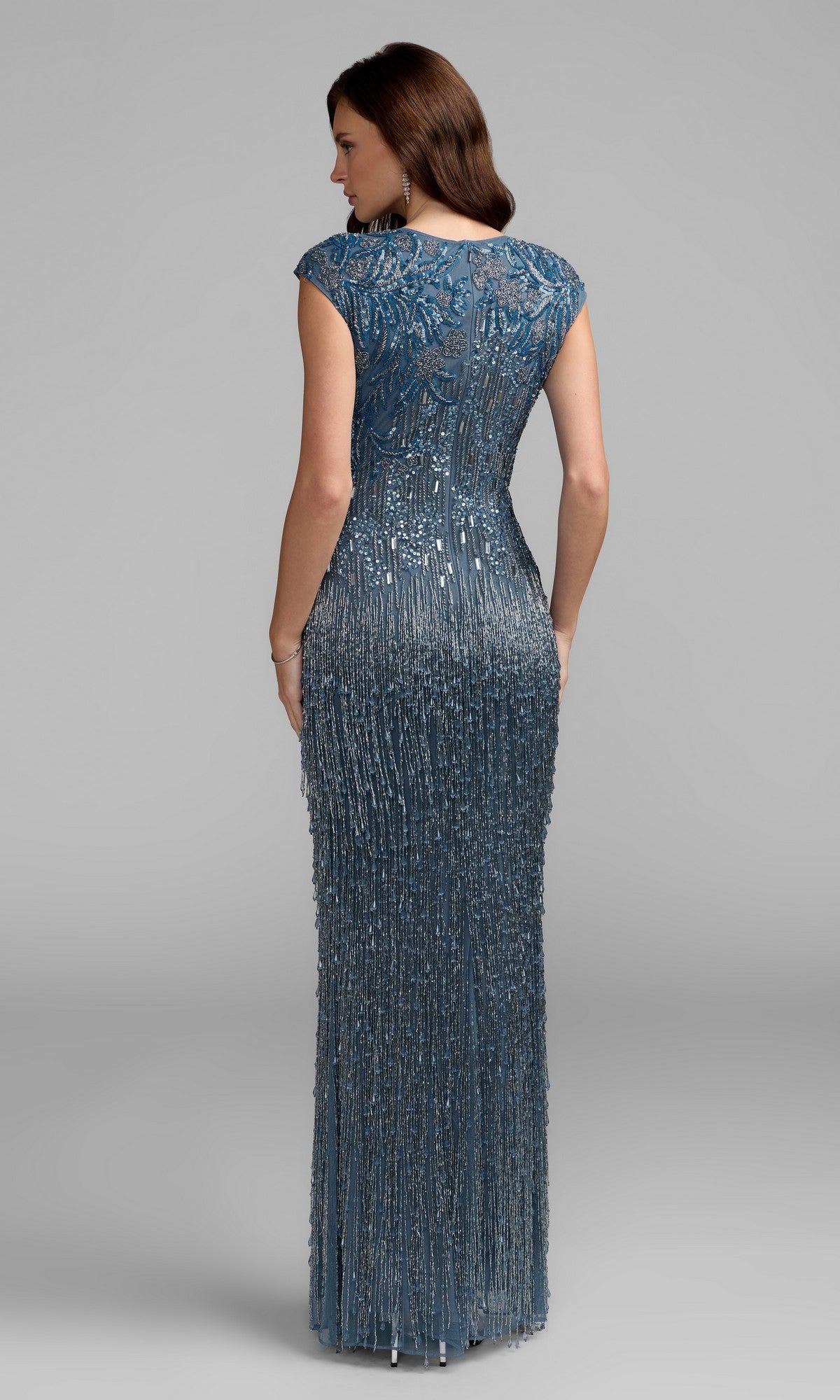 A woman faces away, wearing the Mac Duggal 6169 Beaded Long Lilac Formal Dress with cap sleeves and intricate detailing, set against a plain gray background.